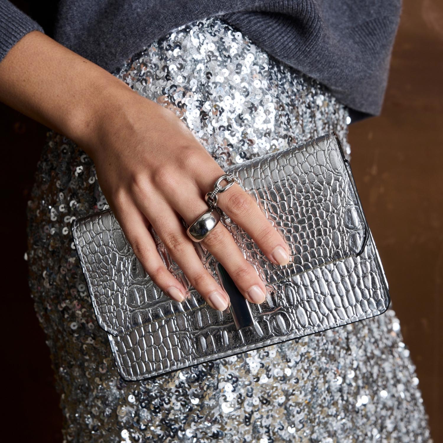 Frau traegt Ring BELLE 20 an Hand mit Silber-Clutch und Sequin-Oberteil
