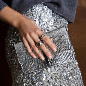 Frau traegt Ring BELLE 21 an der Hand, haelt silberne Clutch