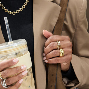 Frau traegt Ring BELLE 21 gold an der Hand, haelt Getraenk