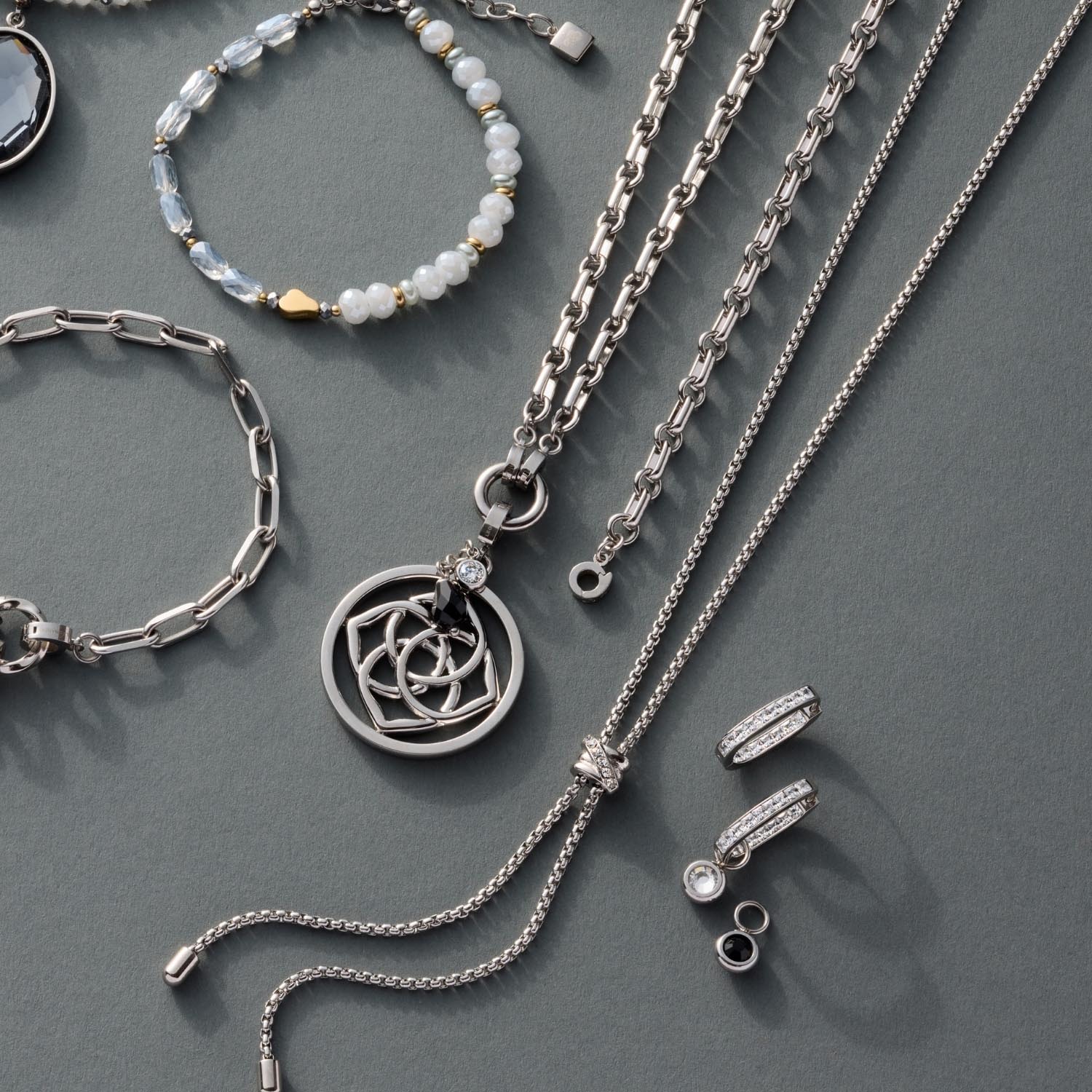 Silberne Creole BOSSY mit weiteren Kettenmodellen und Perlenarmband auf grauem Untergrund