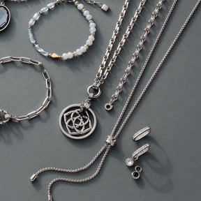 Silberne Creole BOSSY mit weiteren Kettenmodellen und Perlenarmband auf grauem Untergrund
