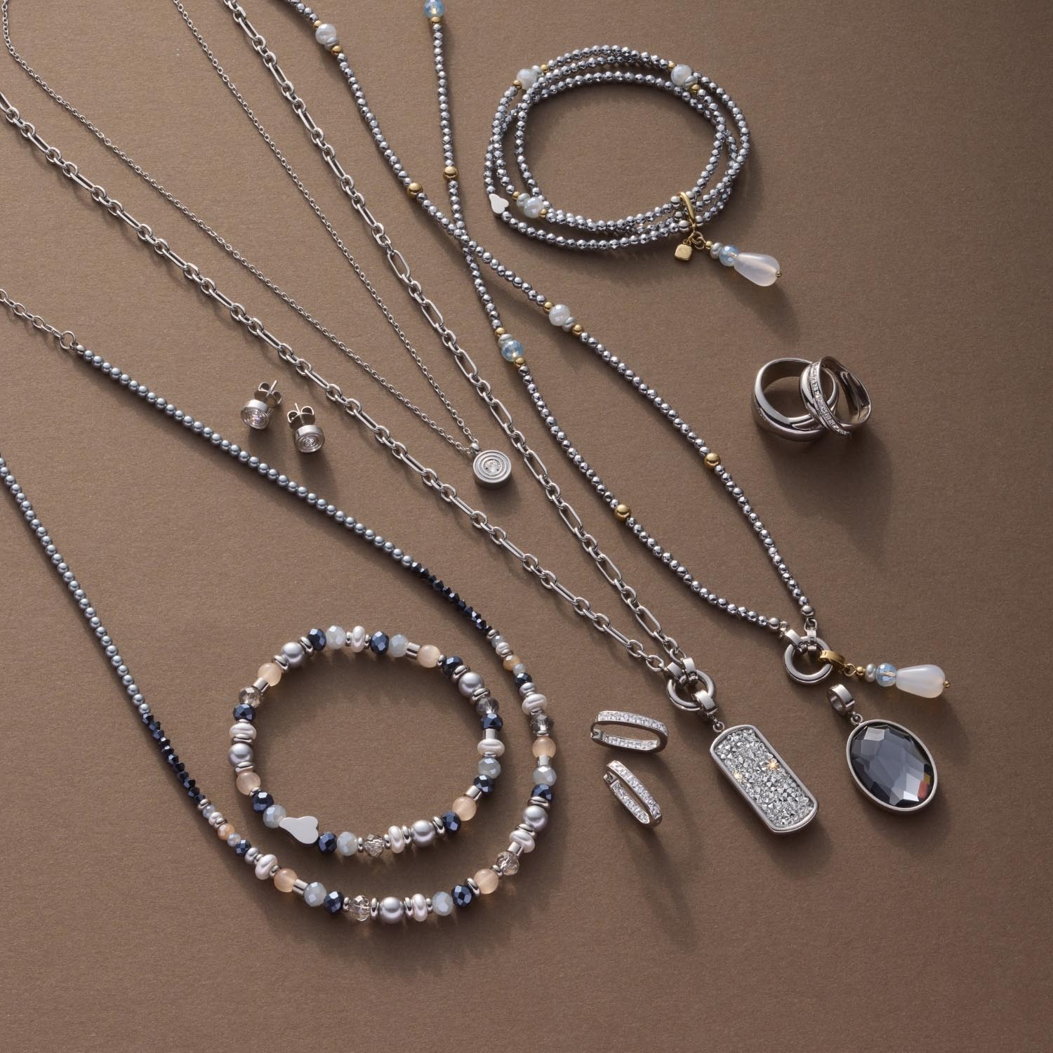 Silberner Schmuck auf beigem Untergrund: Halsketten, Armbänder, Ringe und Anhänger aus Edelstahl mit Zirkonia