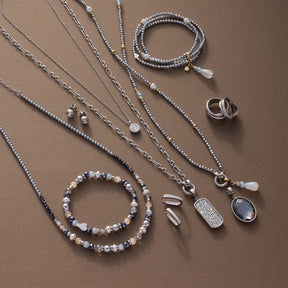 Silberner Schmuck auf beigem Untergrund: Halsketten, Armbänder, Ringe und Anhänger aus Edelstahl mit Zirkonia