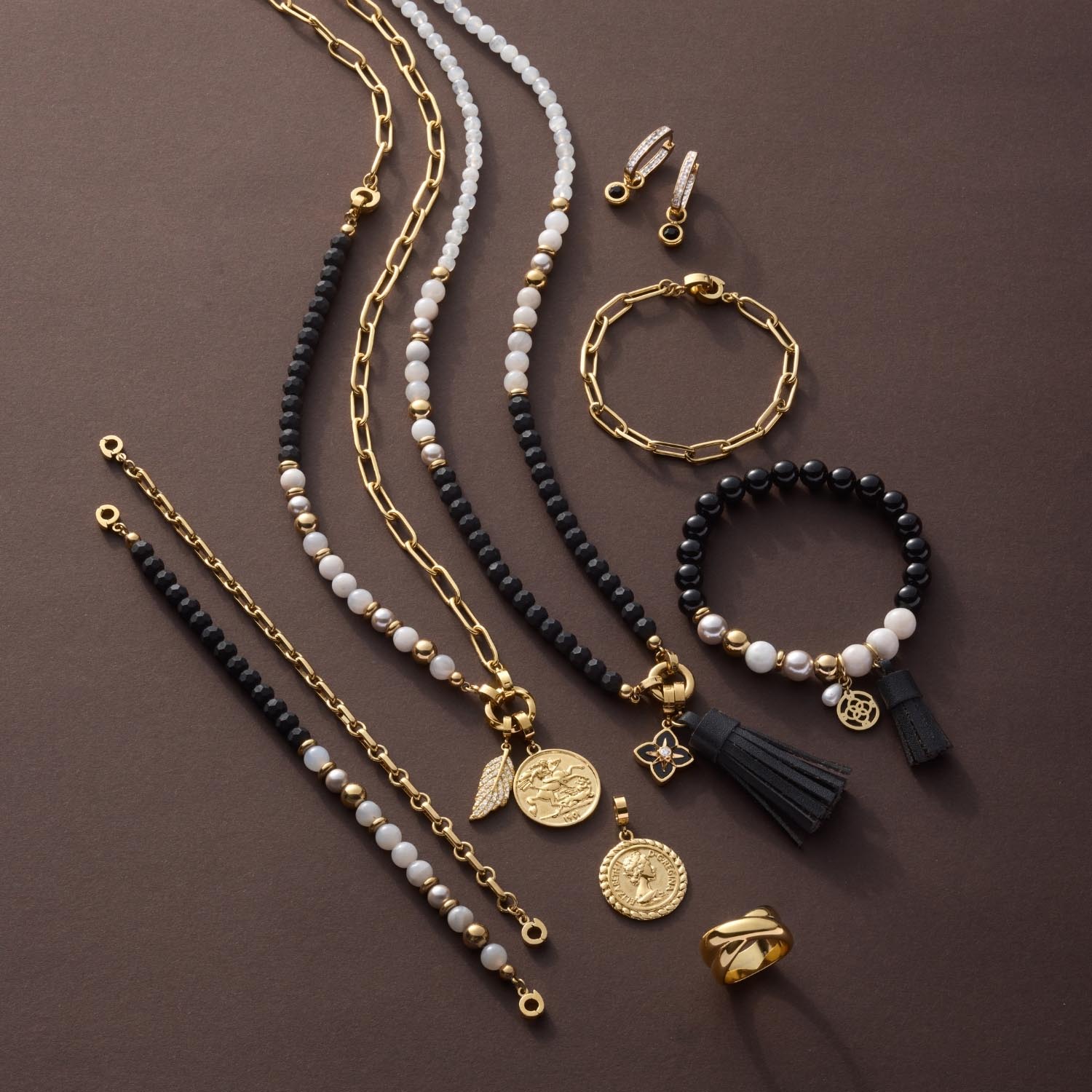 Schmuckkollektion mit Halsketten, Armbändern und Ohrringen in Gold und Schwarz auf grauem Hintergrund