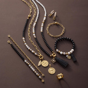 Schmuckkollektion mit Halsketten, Armbändern und Ohrringen in Gold und Schwarz auf grauem Hintergrund