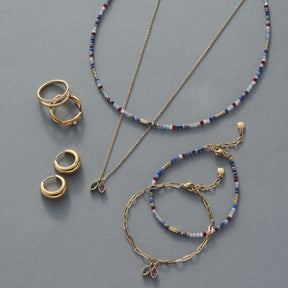Halskette MAY mit Ringen und Armbändern in Gold und Perlen auf grauem Untergrund