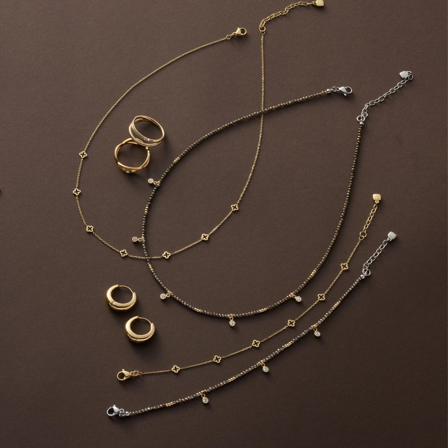 Halskette ANNA, Ringe und Armbänder in Gold und Silber auf braunem Untergrund arrangiert