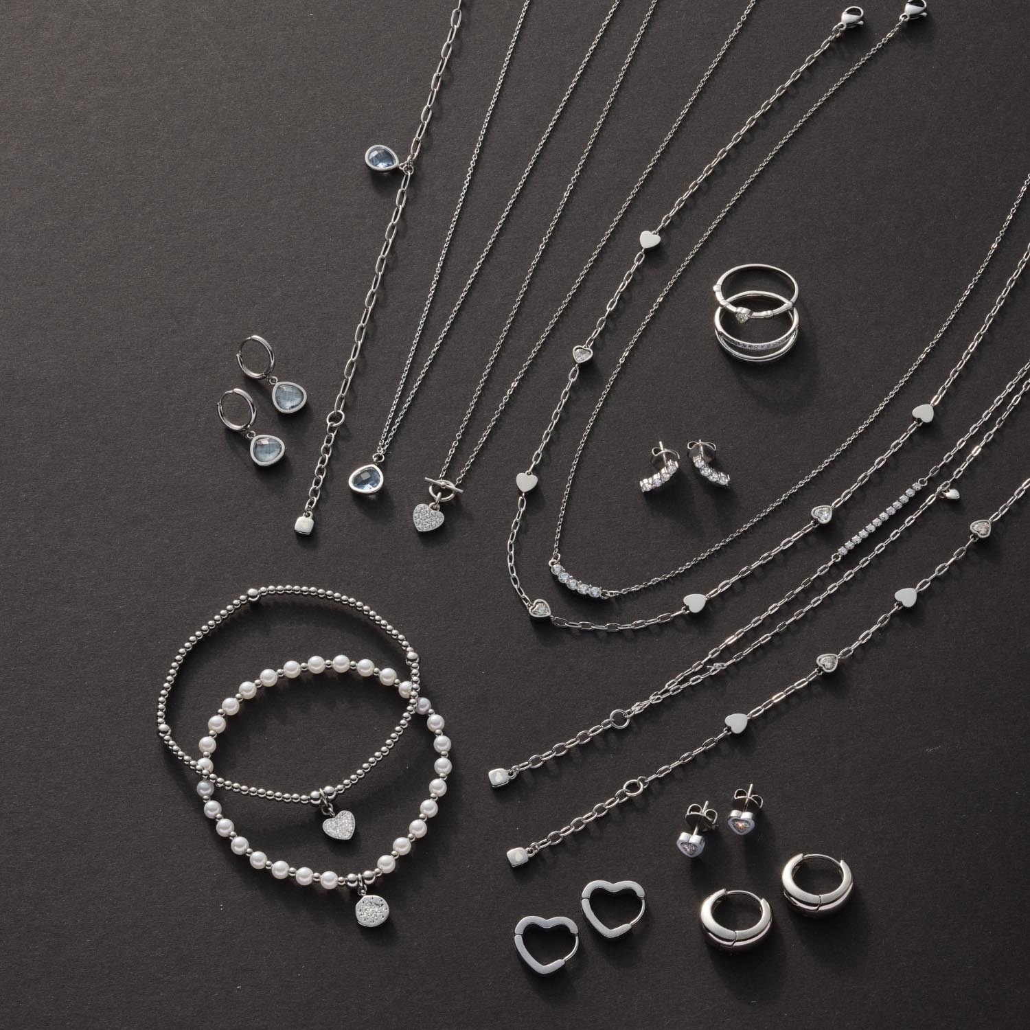 Silberne Halsketten, Armbänder, Ringe und Ohrringe auf schwarzem Hintergrund arrangiert