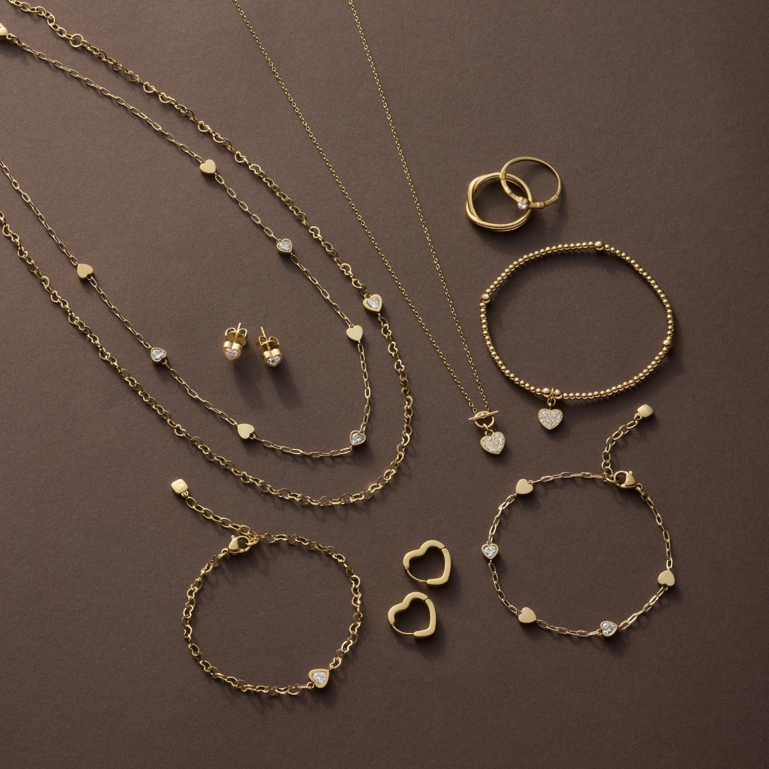 Goldener Schmuck auf braunem Hintergrund: Halsketten, Armbänder, Ringe und Ohrringe