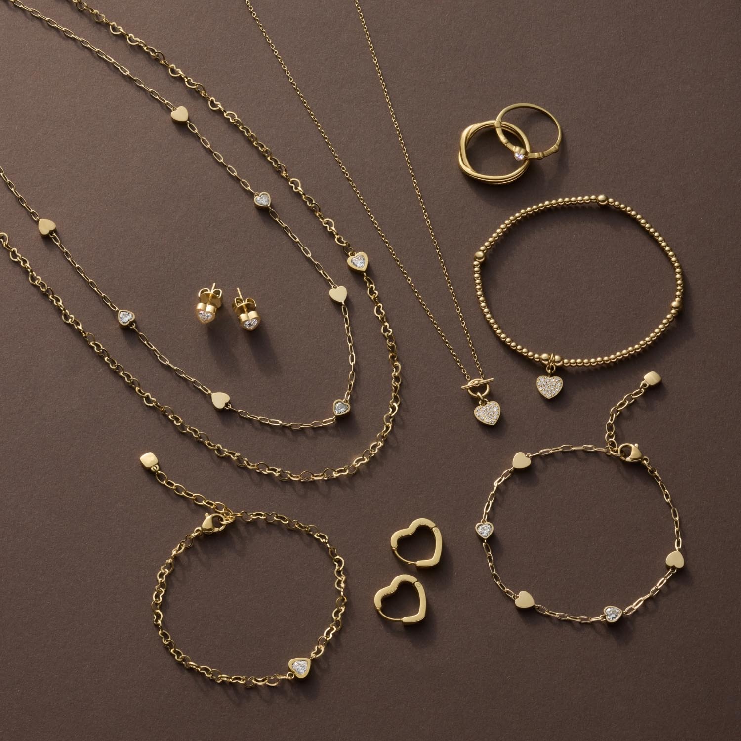 Goldene Schmuckkollektion mit Armbändern, Ketten, Ringen und Ohrringen auf braunem Hintergrund