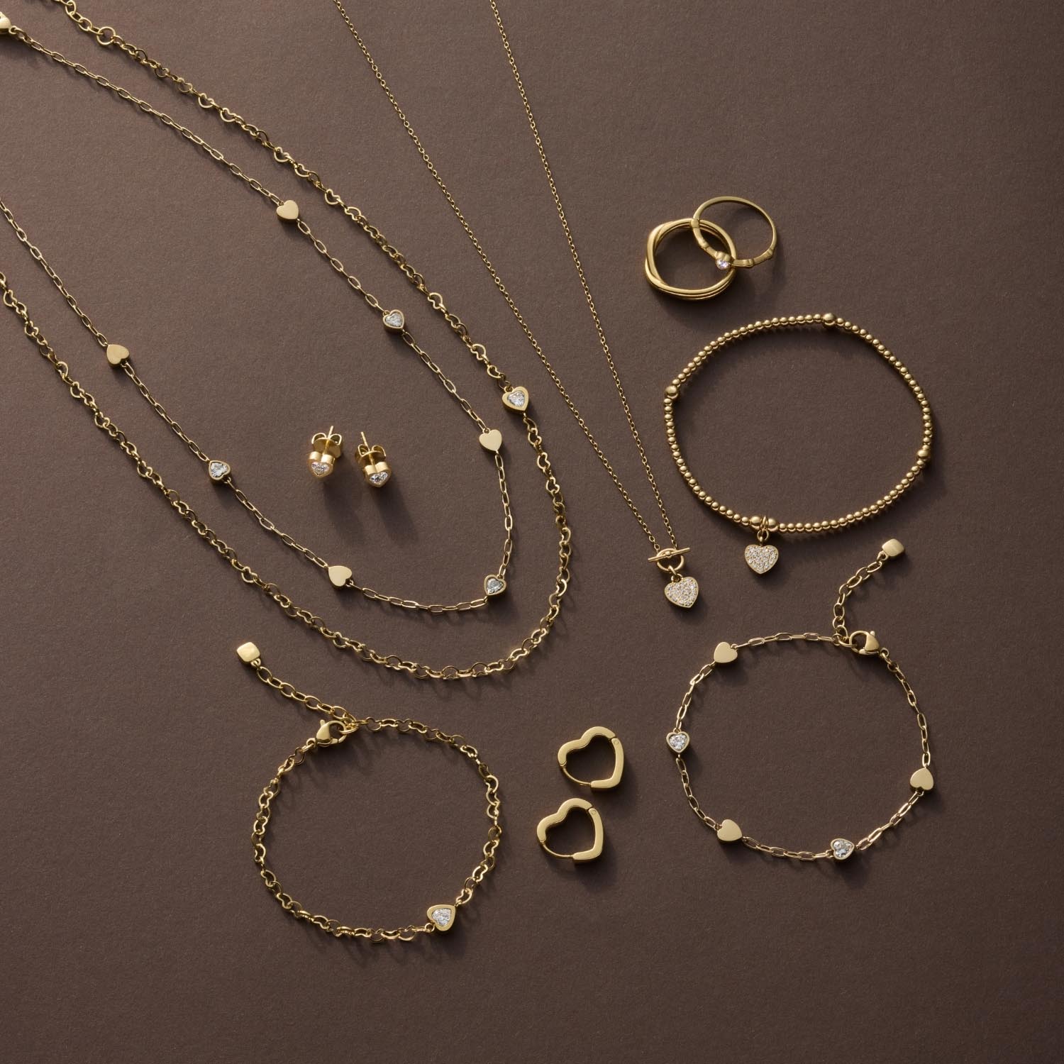 Goldener Schmuck: Halsketten mit Perlen, Armbänder, Ringe und Ohrstecker auf braunem Hintergrund