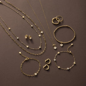Goldener Schmuck: Halsketten mit Perlen, Armbänder, Ringe und Ohrstecker auf braunem Hintergrund