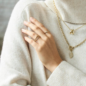 Hand traegt Ring CHRISTIE 17 gold CIAO auf cremefarbener Kleidung mit Halsketten