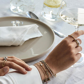 Hand mit Ringen und Armbändern am gedeckten Tisch
