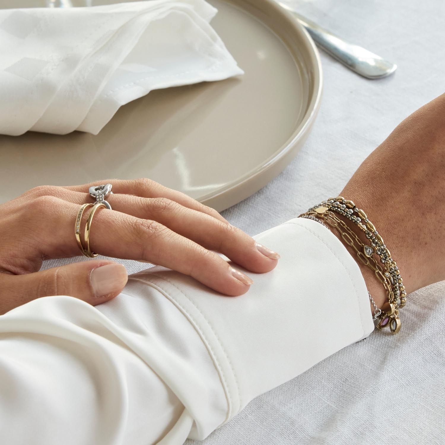 Frau trägt Ring TINI 17 gold und Armband, Hand auf weißem Stoff