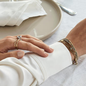 Frau trägt Ring TINI 17 gold und Armband, Hand auf weißem Stoff
