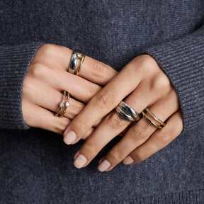 Hände mit mehreren goldenen Ringen, darunter Ring TINI 17 gold CIAO, an grauem Pullover