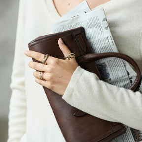 Frau traegt Ring TINI 17 gold an der Hand, haelt Zeitung und braune Handtasche