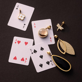 Anhänger DIANA Clip & Mix mit Spielkarten und goldfarbenen Accessoires auf schwarzem Untergrund