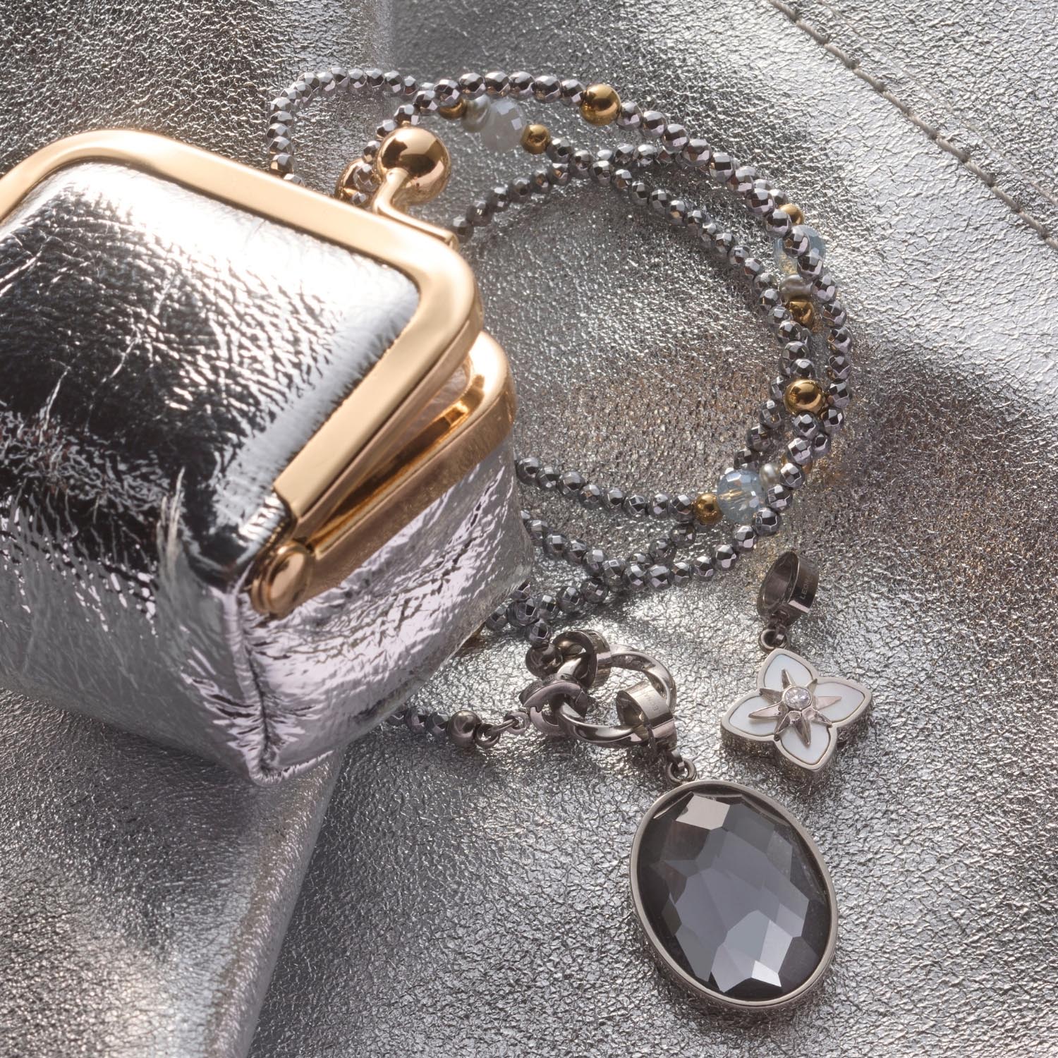 Anhänger REIJA Clip & Mix mit Kette, silberner Kugelkette und grauem Stein neben metallischer Tasche