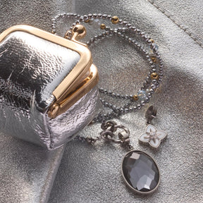 Anhänger REIJA Clip & Mix mit Kette, silberner Kugelkette und grauem Stein neben metallischer Tasche