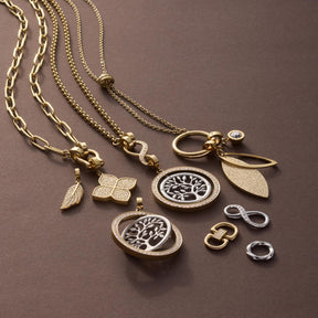 Anhänger FEDRA gold Clip & Mix mit Ketten und austauschbaren Charms auf braunem Untergrund
