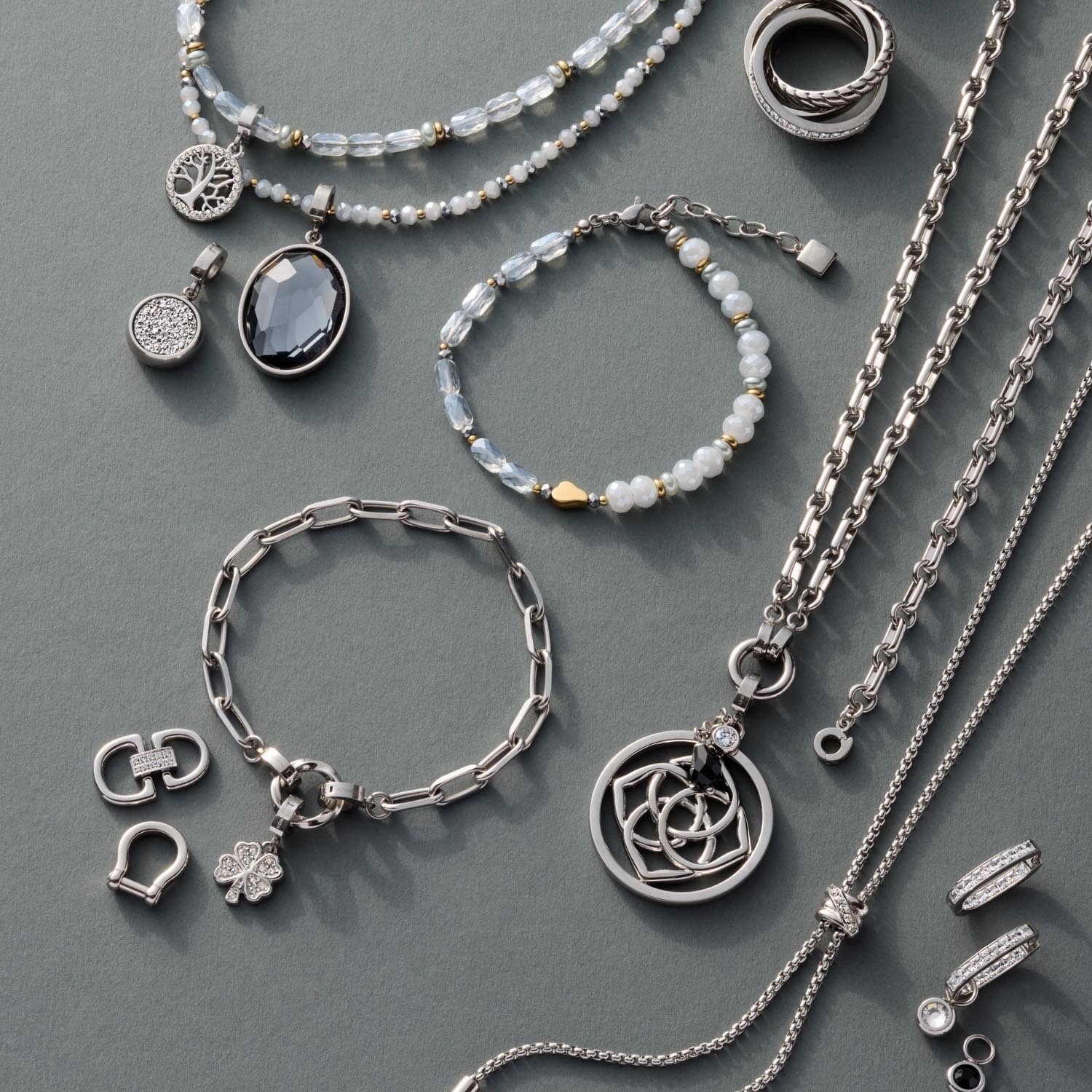 Silberner Schmuck mit Anhängern, Ketten, Armbändern und Ringen auf grauem Hintergrund