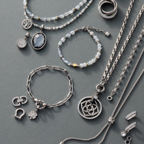 Silberner Schmuck mit Anhängern, Ketten, Armbändern und Ringen auf grauem Hintergrund
