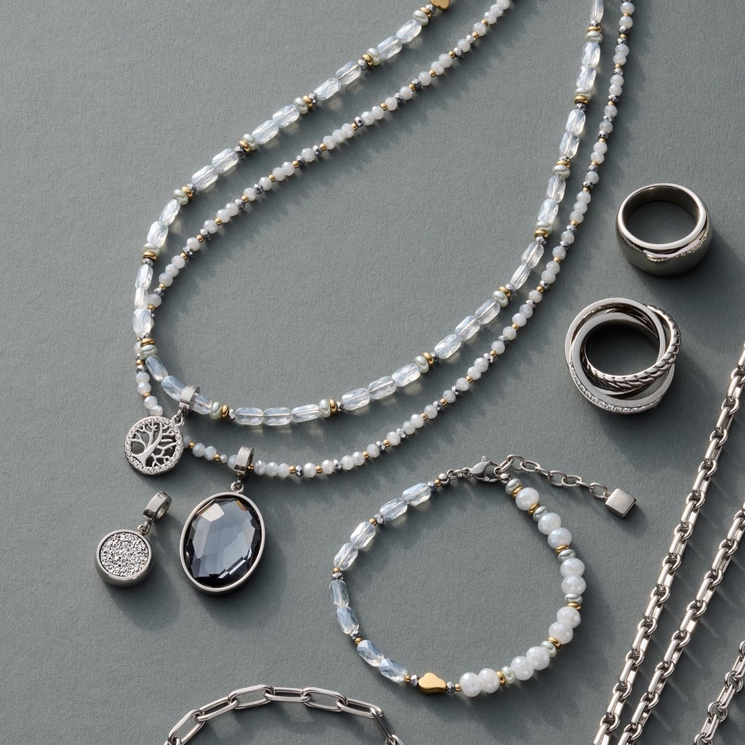Schmuckkollektion mit Perlenketten, Ringen und Anhängern auf grauem Hintergrund