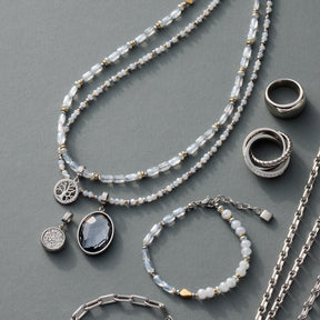 Schmuckkollektion mit Perlenketten, Ringen und Anhängern auf grauem Hintergrund