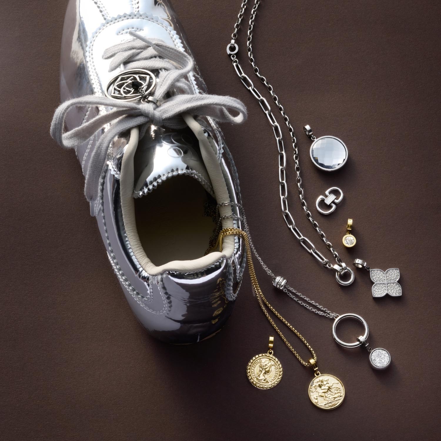 Weiße Sneaker mit offener Zunge, daneben silberne und goldene Schmuckanhänger arrangiert