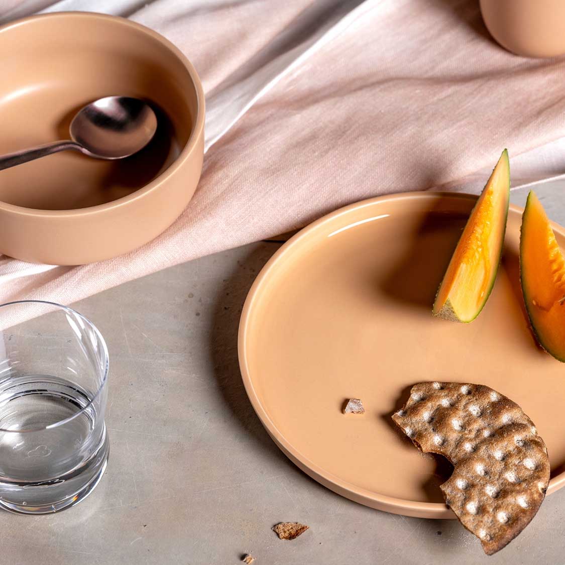 Keramikteller ROMA apricot mit Orangenscheiben, Keks und Wasser auf Tisch