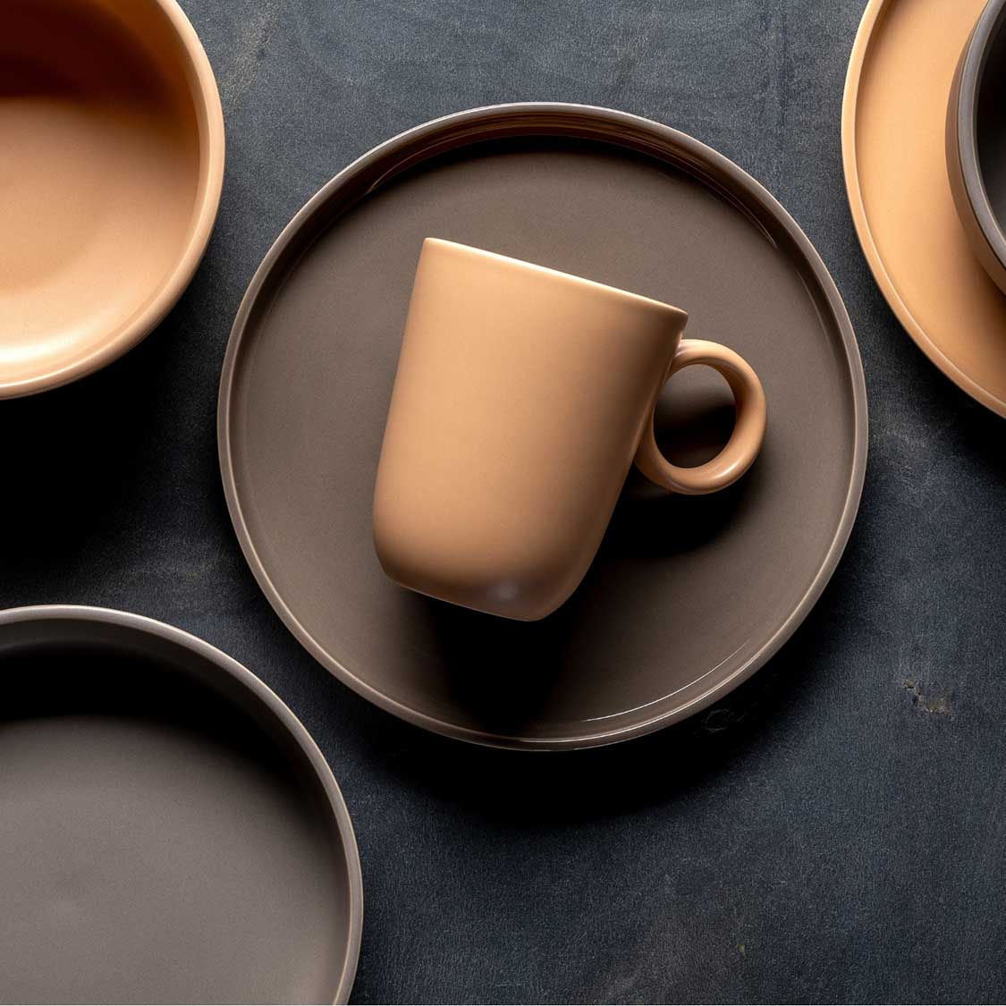 Keramiktasse ROMA apricot auf grauem Teller mit weiteren Tassen und Tellern