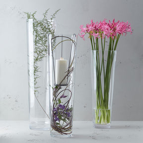 Drei klare Glasvasen mit Blumenarrangements auf weißer Oberfläche