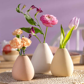 Drei Keramikvasen mit Blumen auf Tisch vor violettem Hintergrund