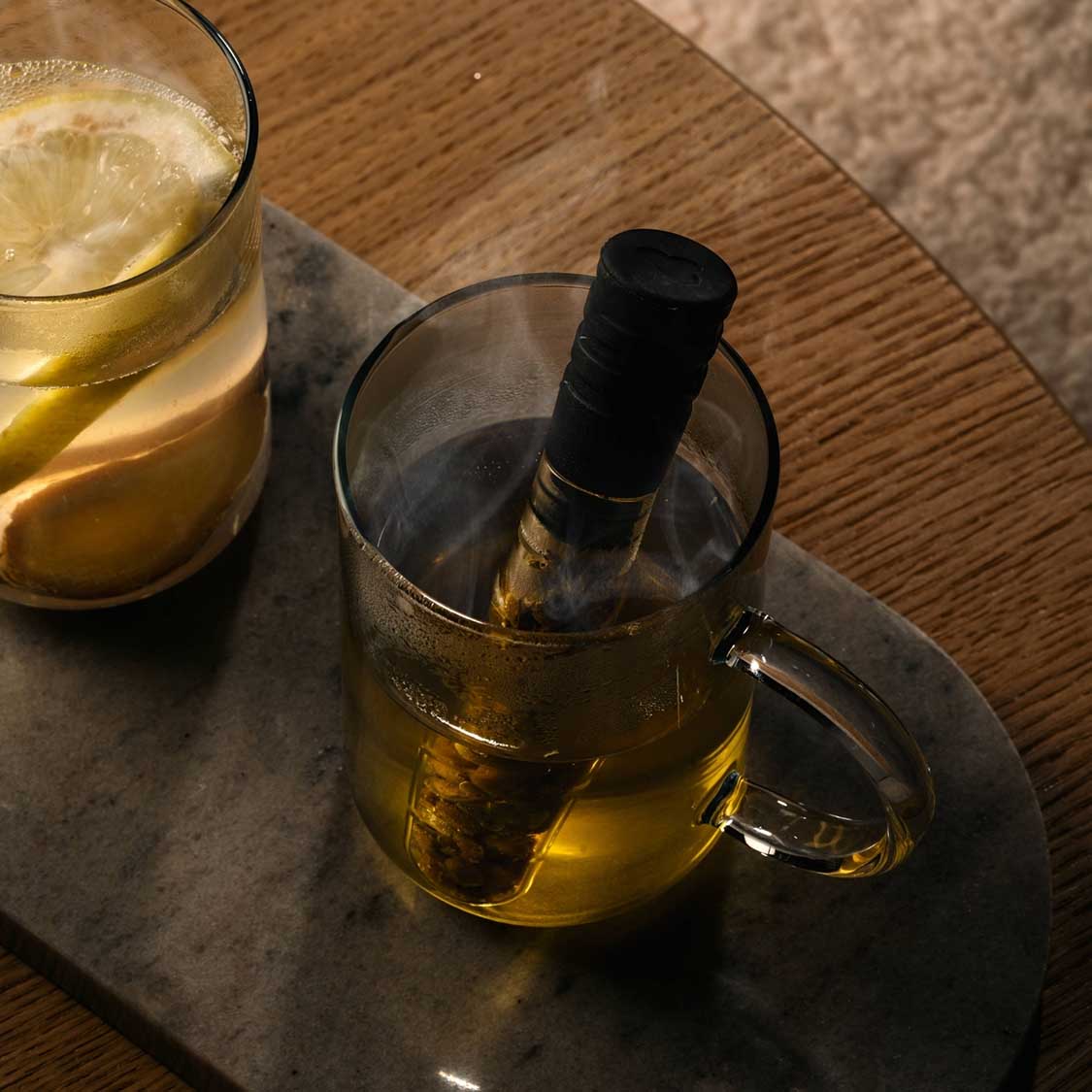 Teeglas NOVO mit heißem Tee und Teekanne auf Marmortablett, daneben gefülltes Glas