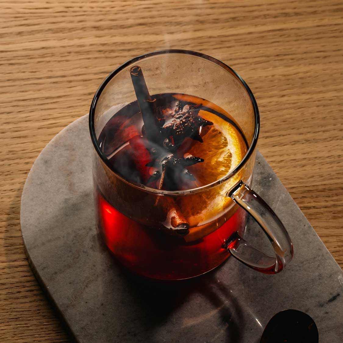 Teeglas NOVO mit Glühwein, Beeren und Zimtstange auf Holztisch