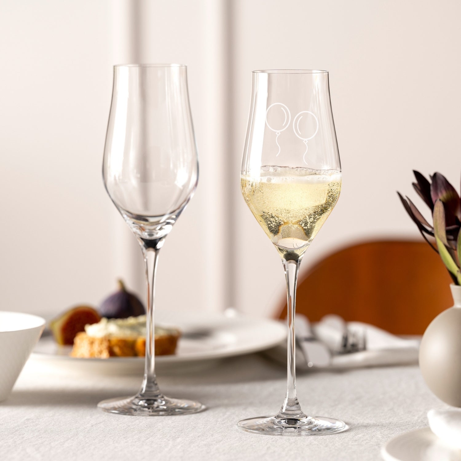 Zwei Champangergläser BRUNELLI auf gedecktem Tisch, eines leer, eines mit Champagner gefüllt, mit Gravur