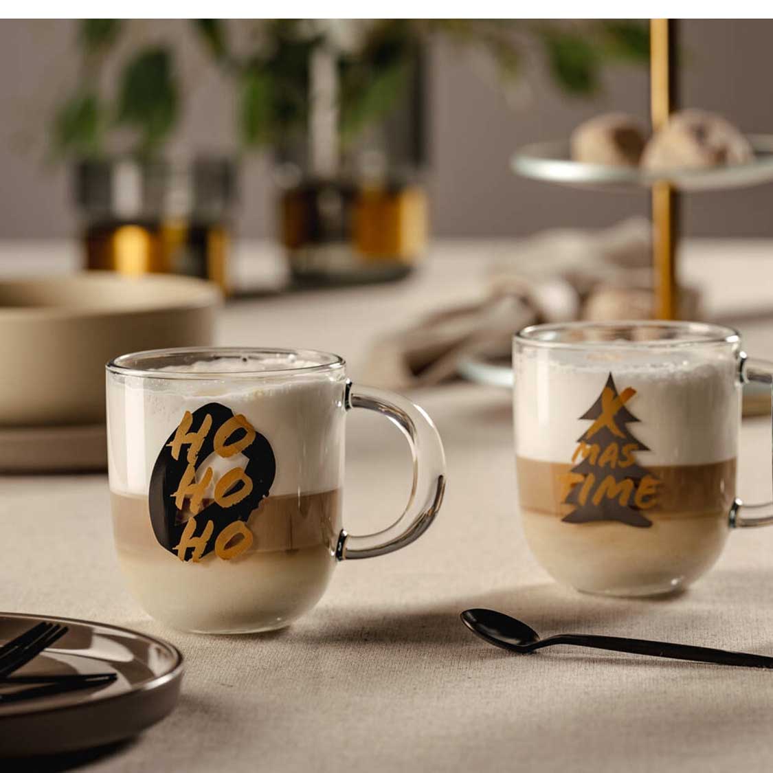 Zwei Glastassen SILENZIO mit schwarzem HO HO HO Aufdruck auf Tisch mit Besteck