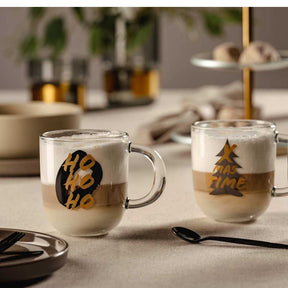 Zwei Glastassen SILENZIO mit schwarzem HO HO HO Aufdruck auf Tisch mit Besteck