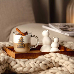 Tasse SILENZIO mit Weihnachtsmotiv auf Holztablett, Zimtstangen, weiße Dekofiguren, gemütliches Wohnzimmer