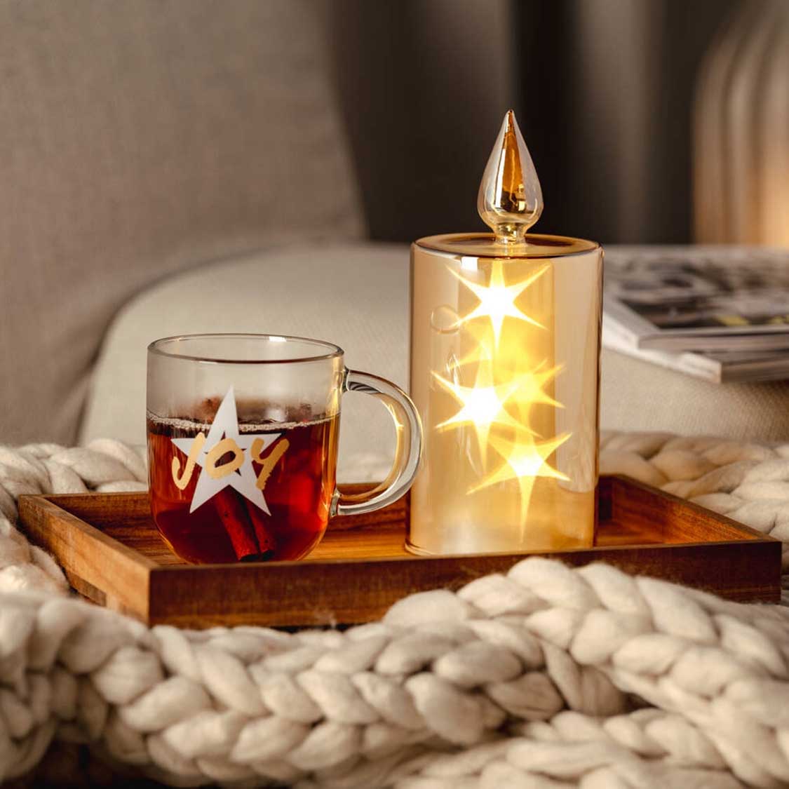 Glastasse mit Sternen-Gravur auf Holzbrett mit Kerze und Tee