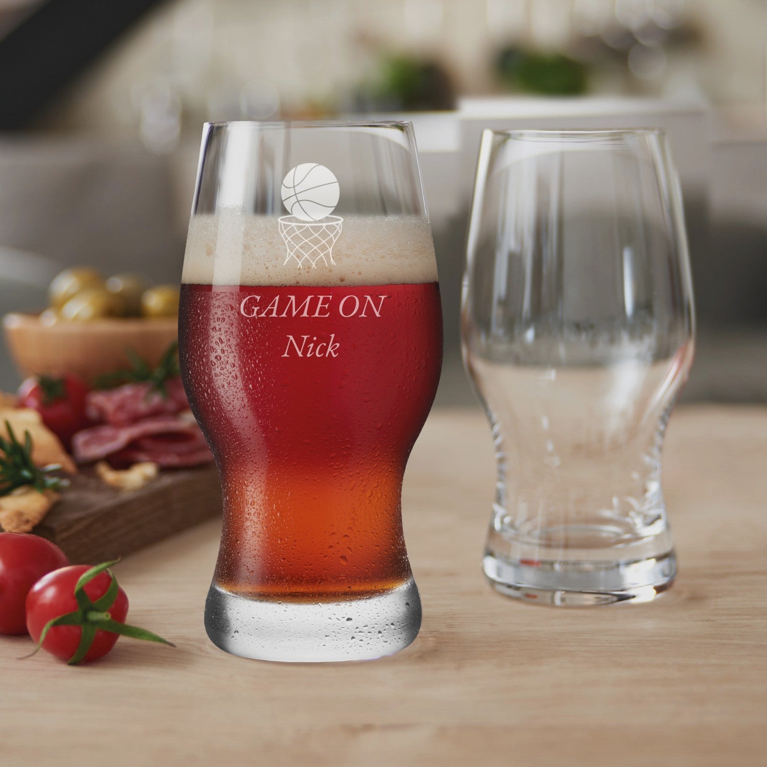 Bierglas TAVERNA mit rotem Getränk und Gravur "GAME ON Nick", daneben leeres Glas, Küchentheke mit Gemüse