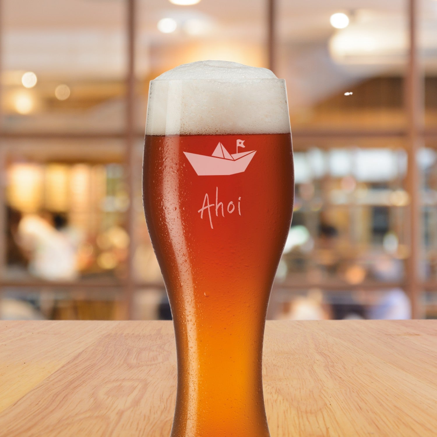 Weizenbierglas TAVERNA mit Gravur Ahoi und Papierschiff, gefüllt mit Bier, auf Holztisch