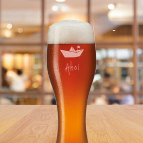 Weizenbierglas TAVERNA mit Gravur Ahoi und Papierschiff, gefüllt mit Bier, auf Holztisch
