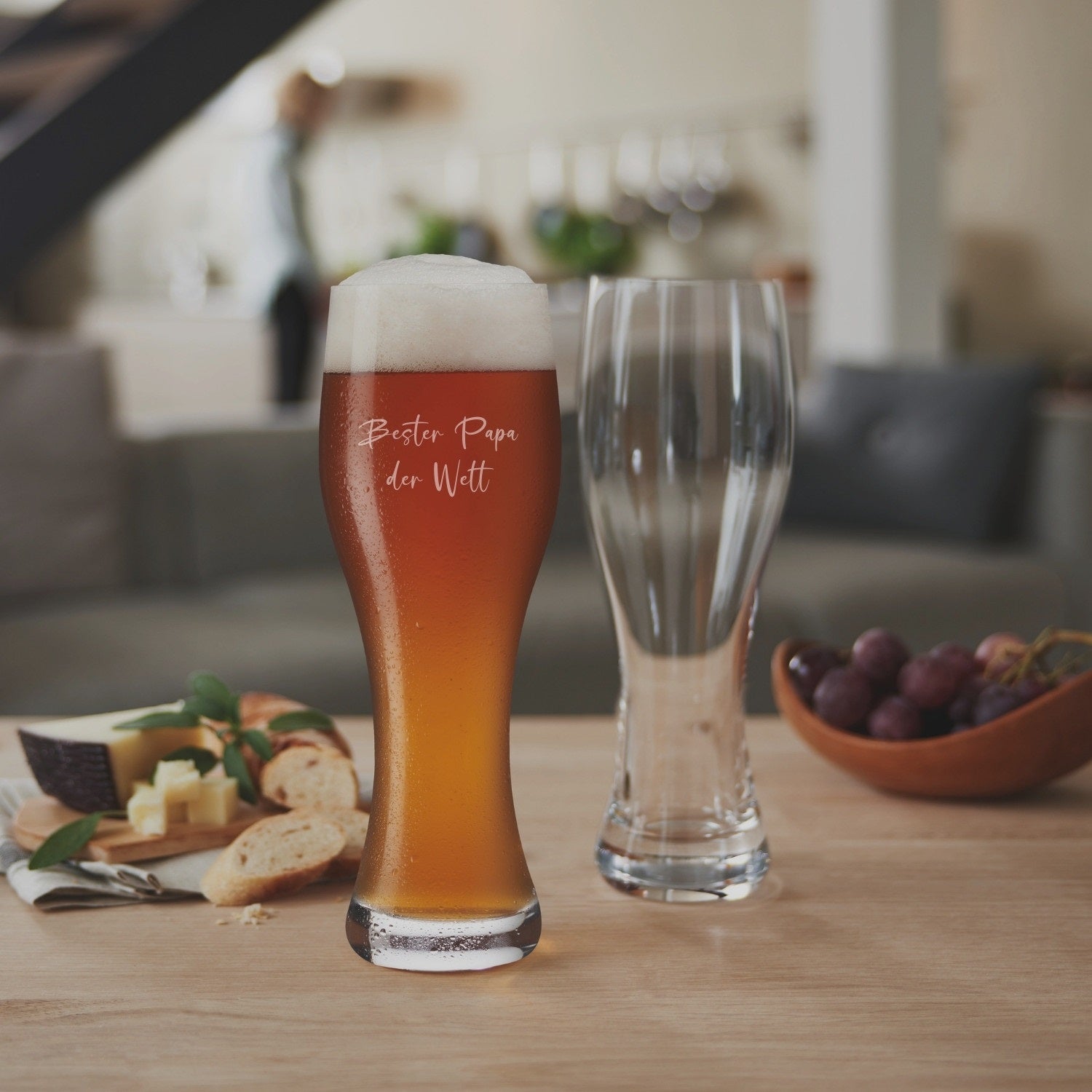 Weizenbierglas TAVERNA mit Gravur, gefüllt mit Bier, auf Holztisch in Wohnraum