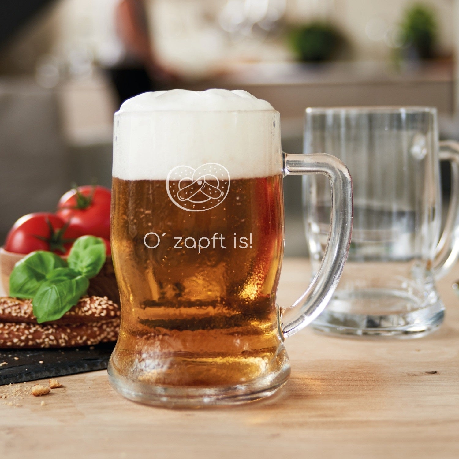 Bierseidel TAVERNA mit Bier gefüllt auf Holztisch, Gravur sichtbar, Tomaten und Brezel daneben