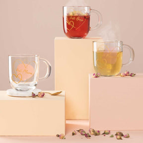 Drei Glastassen EMOZIONE mit Tee auf gestaffelten Boxen, getrocknete Rosenblüten als Deko