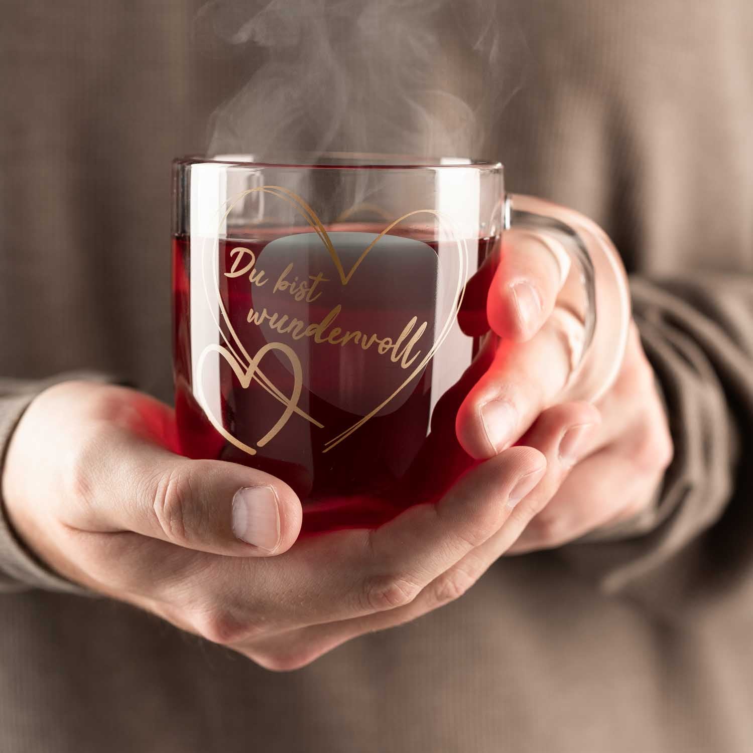 Person hält dampfende Glastasse mit Gravur "Du bist wundervoll