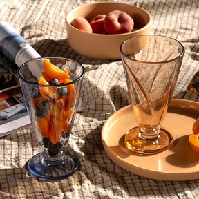 Eisbecher CONO gefüllt mit Getränk und Früchten auf sonnigem Terrassentisch, daneben Obstschale und leeres Glas